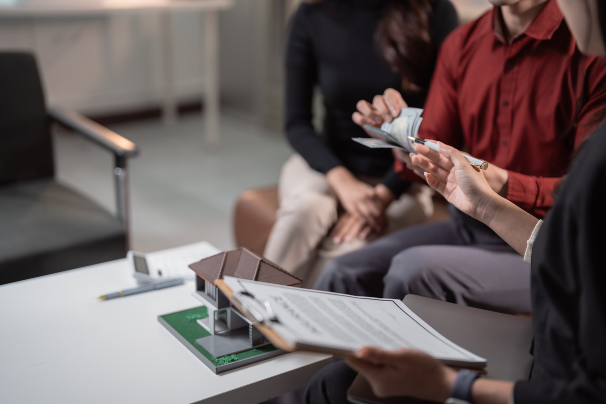 Paar mit Geldscheinen wird von Maklerin beraten